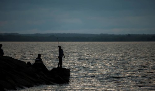 A person fishing on a rocky shore at dusk with a calm lake in Ottawa, Ontario, Canada, North
