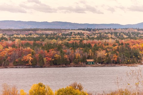 A small cabin nestled in an autumn forest along the Ottawa River with hills in the distance in