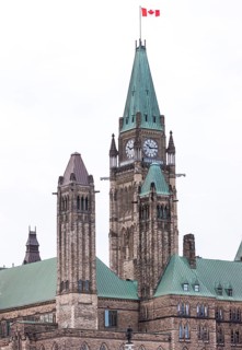 The Canadian parliament building with a clock tower and green roof under an overcast sky in Ottawa,