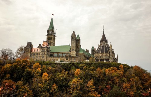 The Canadian Parliament building on a hill surrounded by colorful autumn trees, showcasing gothic
