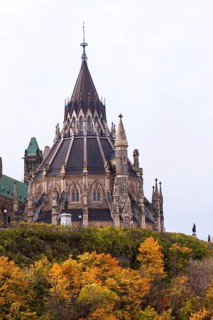 A Gothic-style Canadian Parliament building with a prominent spire, surrounded by colorful autumn