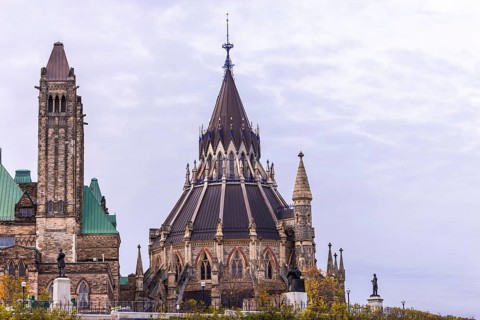 The Canadian Parliament Buildings with an ornate spire and towers against a cloudy sky, showcasing