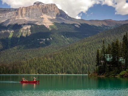 Canoe on Emerald Lake encircled by the Canadian Rocky Mountains and dense forest under a bright sky