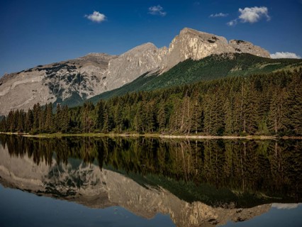 Mountainous landscape of the Canadian Rocky Mountains with dense forest reflected in a calm lake