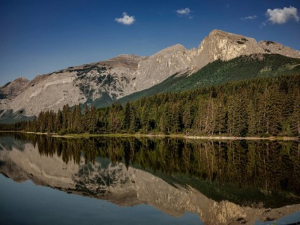Quiet, reflective waters mirror the surrounding Canadian Rocky Mountains and forest near Canmore,