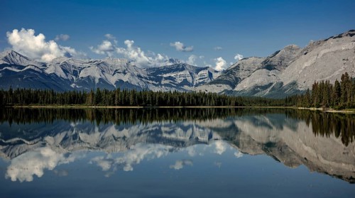 Majestic mountains of the Canadian Rocky Mountains and forest reflected in calm lake under a clear