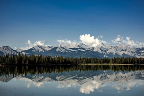 Clear reflections of mountain peaks of the Canadian Rocky Mountains in a lake under fluffy clouds