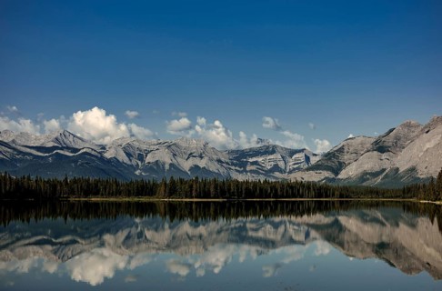 A pristine lake reflecting cloud-capped mountains of the Canadian Rocky Mountains and a peaceful
