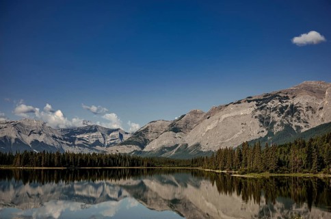 Reflections of rugged mountains of the Canadian Rocky Mountains in a calm lake framed by dense