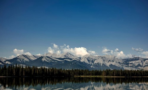 Majestic mountain range of the Canadian Rocky Mountains mirrored in a tranquil lake under a vast