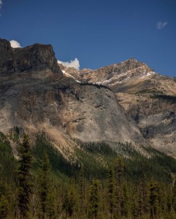 Mountain peaks of the Canadian Rocky Mountains with patches of snow and a forested base under a