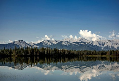 Tranquil lake mirroring mountains of the Canadian Rocky Mountains and sky, with pine forest and