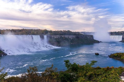 Wide view of the Bridal Veil Falls and the Horseshoe Falls with mist rising under a partly cloudy