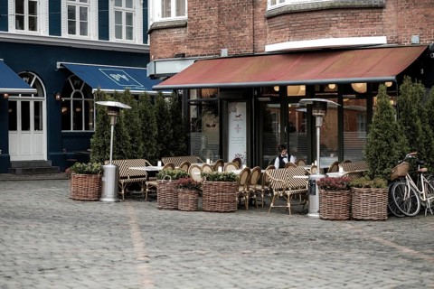 An empty outdoor cafe with wicker chairs and planters on a cobblestone pavement in Aarhus, Denmark,