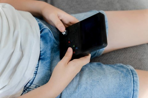 Child hands holding and playing portable video game console during leisure time