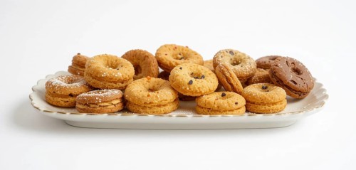 A variety of cookies, some with chocolate chips and powdered sugar, are arranged on a white,