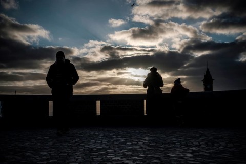Silhouetted figures at sunset with dramatic clouds and a distant tower in Helsingborg, Sweden,