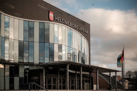 Helsingborg Arena featuring a glass facade, flags, and situated under cloudy weather in