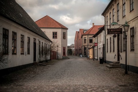 An empty street lined with buildings under a cloudy sky, vintage signs adding to the quiet