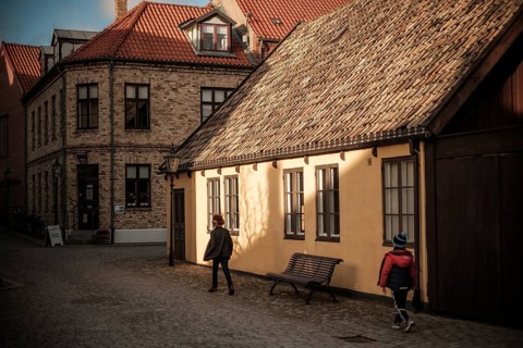 A quiet street with brick buildings and tile roofs, bathed in warm autumn light and shadows in