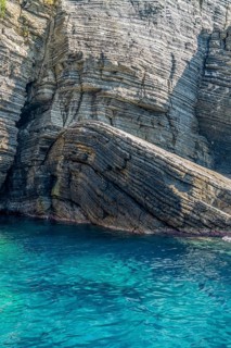 Sunny illuminated detail of the ligurian coast showing a layered rock formation and blue sea