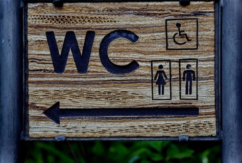 Wooden sign indicating direction of public toilet facilities for all users in ronda, malaga, spain
