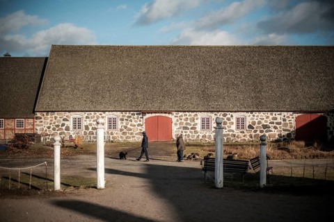 Stone building with red doors on a farm, people walking dogs in foreground in Helsingborg, Sweden,