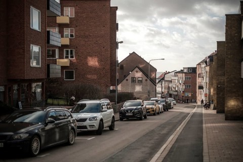 Quiet residential street with parked cars and brick buildings under clouds in Helsingborg, Sweden,