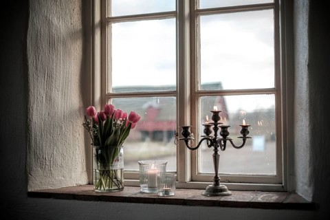 Window ledge adorned with tulips and a candlestick, providing a rustic view of the exterior in