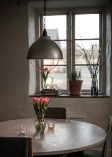 A cozy table setting with tulips and a soft glow from a pendant light, framed by a window in