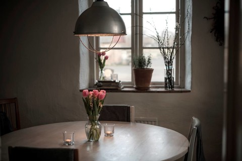 A cozy dining area with a round table, tulips in a vase, and soft lighting from a pendant lamp in