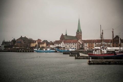 A harbor with docked boats and a church in the background on a cloudy day in Helsingor, Denmark,