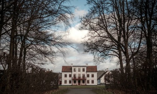 Grand manor house framed by bare trees under a blue sky in Helsingborg, Sweden, Scandinavia
