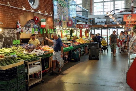 Indoor St. Lawrence Market scene with people browsing stalls filled with colorful produce in