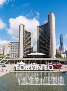 Toronto sign by a fountain against a backdrop of Toronto City Hall at Nathan Phillips Square in
