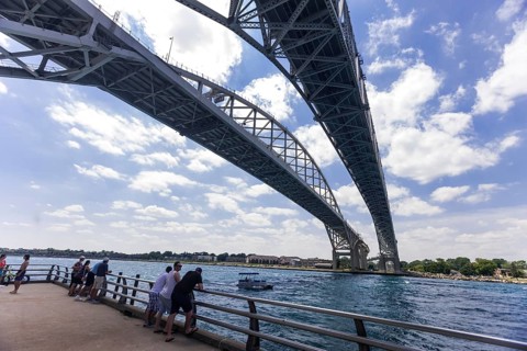 Viewers on a riverside pier looking at the expanse of the Blue Water Bridge connecting Canada and