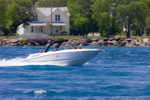 A speedboat glides quickly across the water with trees and houses in the background along the St.