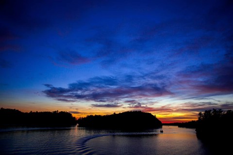 Boat sails on a serene lake during sunset, creating a vivid twilight sky in Muskoka, Ontario,