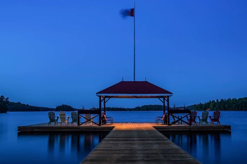 A tranquil lakeside dock with chairs and a flag at dusk in Muskoka, Ontario, Canada, North America