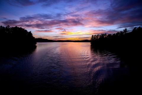 Calm water reflects a colorful evening sky, creating a peaceful twilight landscape in Muskoka,
