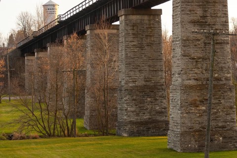 Image of a stone bridge structure with green grass and trees, highlighted by warm tones in St.