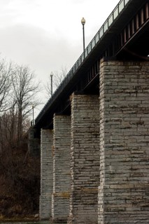 Image of a bridge with massive stone columns under an overcast sky, creating a somber industrial