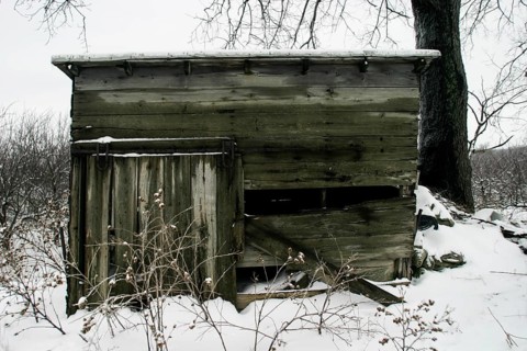 Weathered wooden cabin sits idle in a snowy landscape, conveying abandonment in London, Ontario,