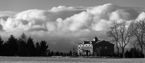 Monochrome image featuring a house against a backdrop of billowing clouds, evoking a serene winter