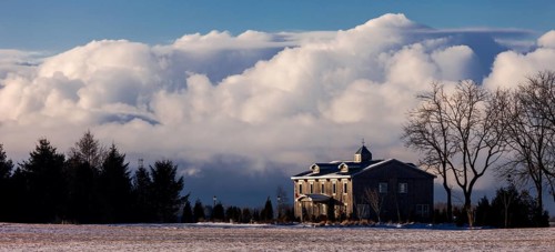 Color image of a house with large clouds in the background, set in a tranquil winter landscape in