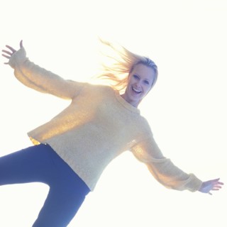 A smiling woman in casual clothes with a bright, light-filled background creating a joyful