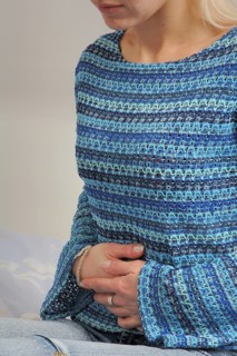Young woman suffering, A woman in a blue striped sweater sitting indoors, clutching her hands over