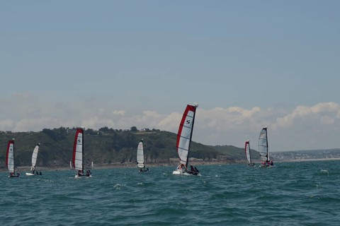 Sailboats glide on the ocean near a hilly coastline under a clear sky, in Brittany, France