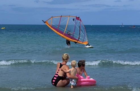 Family at the beach watching windsurfing. Two children with an adult, enjoying the sunny day