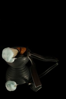 Shaving brush with cream and straight razor reflecting on a black background